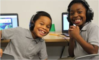 Two young boy students sitting at a desk with computers smiling